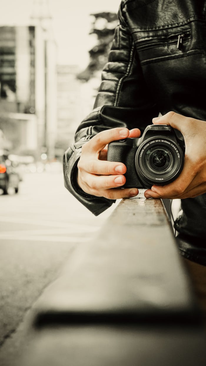 Photographer's hands holding a digital camera in an urban setting.